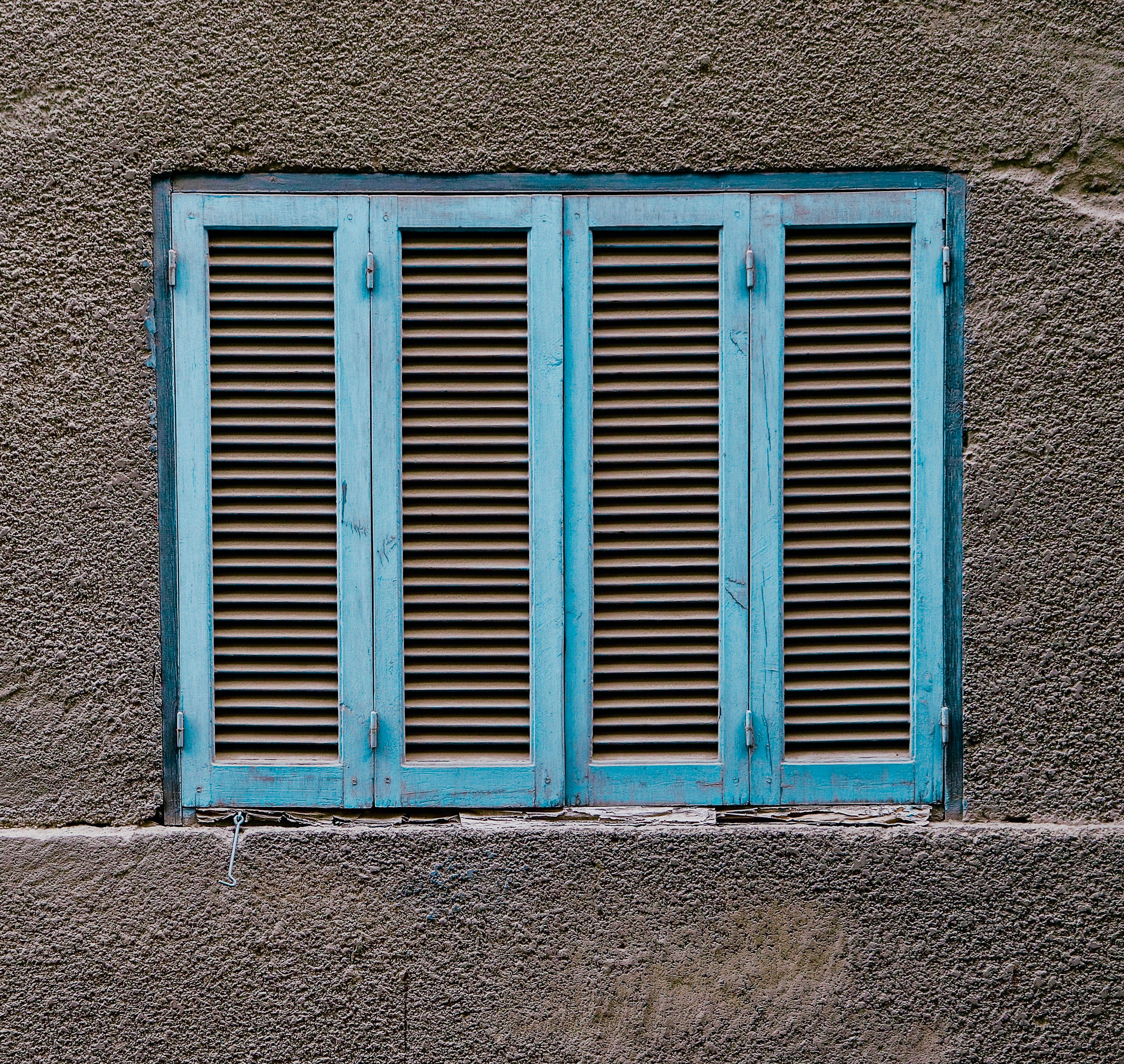 A rustic blue shuttered window set against a textured grey wall, perfect for architecture themes.