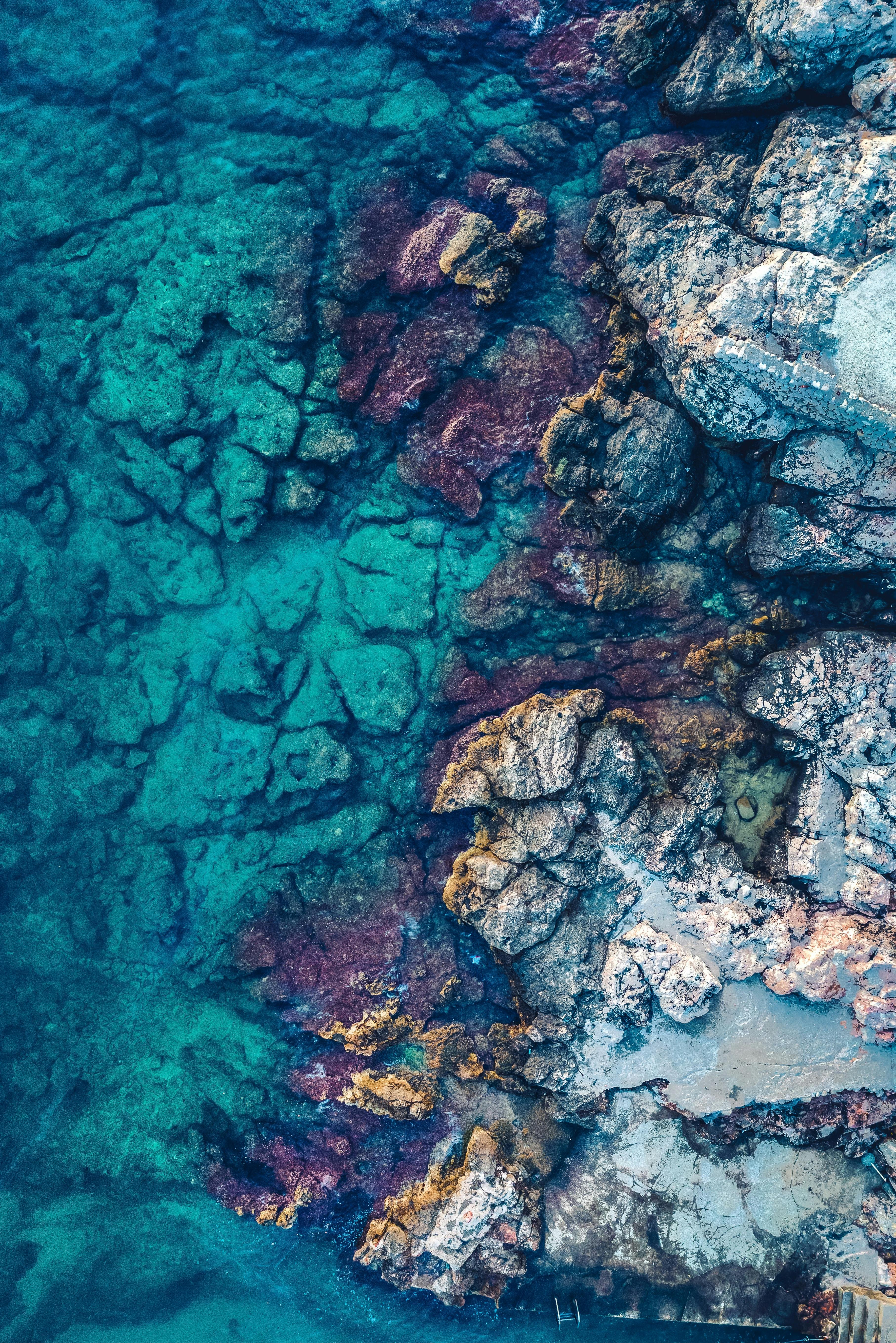 A breathtaking aerial shot of vivid shoreline rocks meeting crystal clear waters, showcasing nature's beauty.