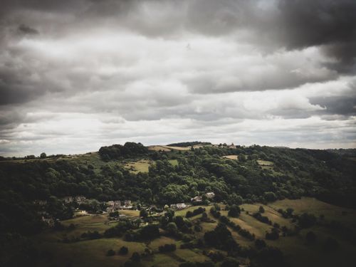 Free A scenic aerial view of a rural countryside with dark clouds and lush greenery. Stock Photo