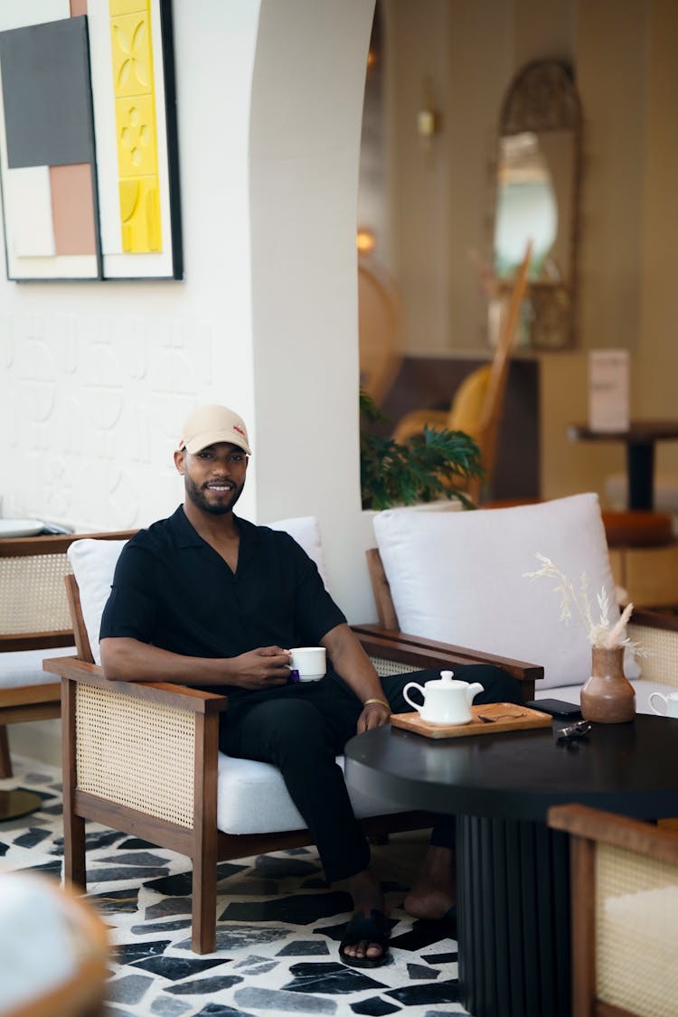 Man Sitting By Cafe Table On Outdoor Couch Drinking Coffee