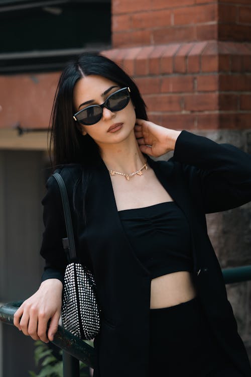 Young Brunette in a Black Outfit and Sunglasses Posing Outside 