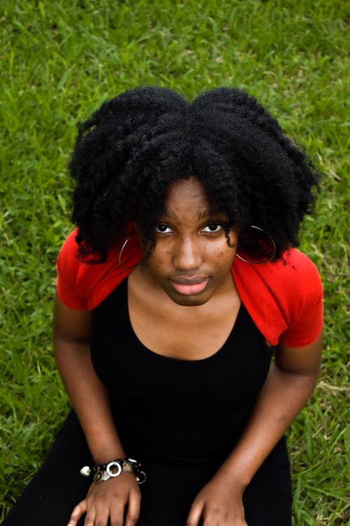 Free Portrait of a woman with natural hair sitting on grass, taken from above. Bright and engaging. Stock Photo