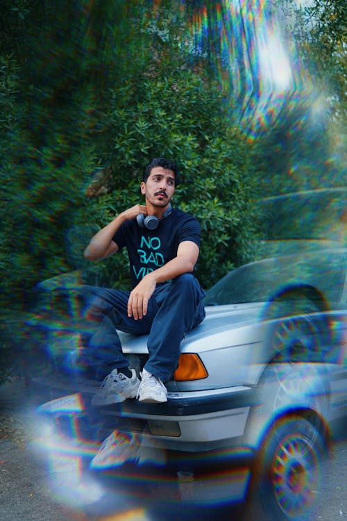 Man with Headphones on Neck Sitting on Car Bonnet