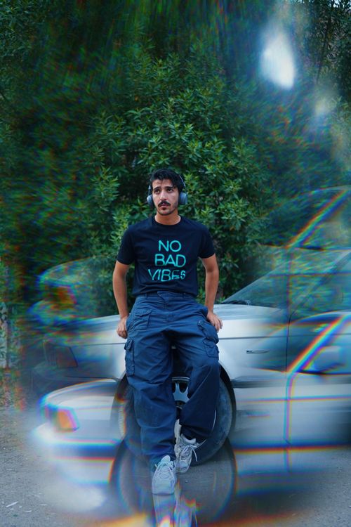 Free A man sitting on a car hood wearing headphones and a 'No Bad Vibes' shirt. Stock Photo