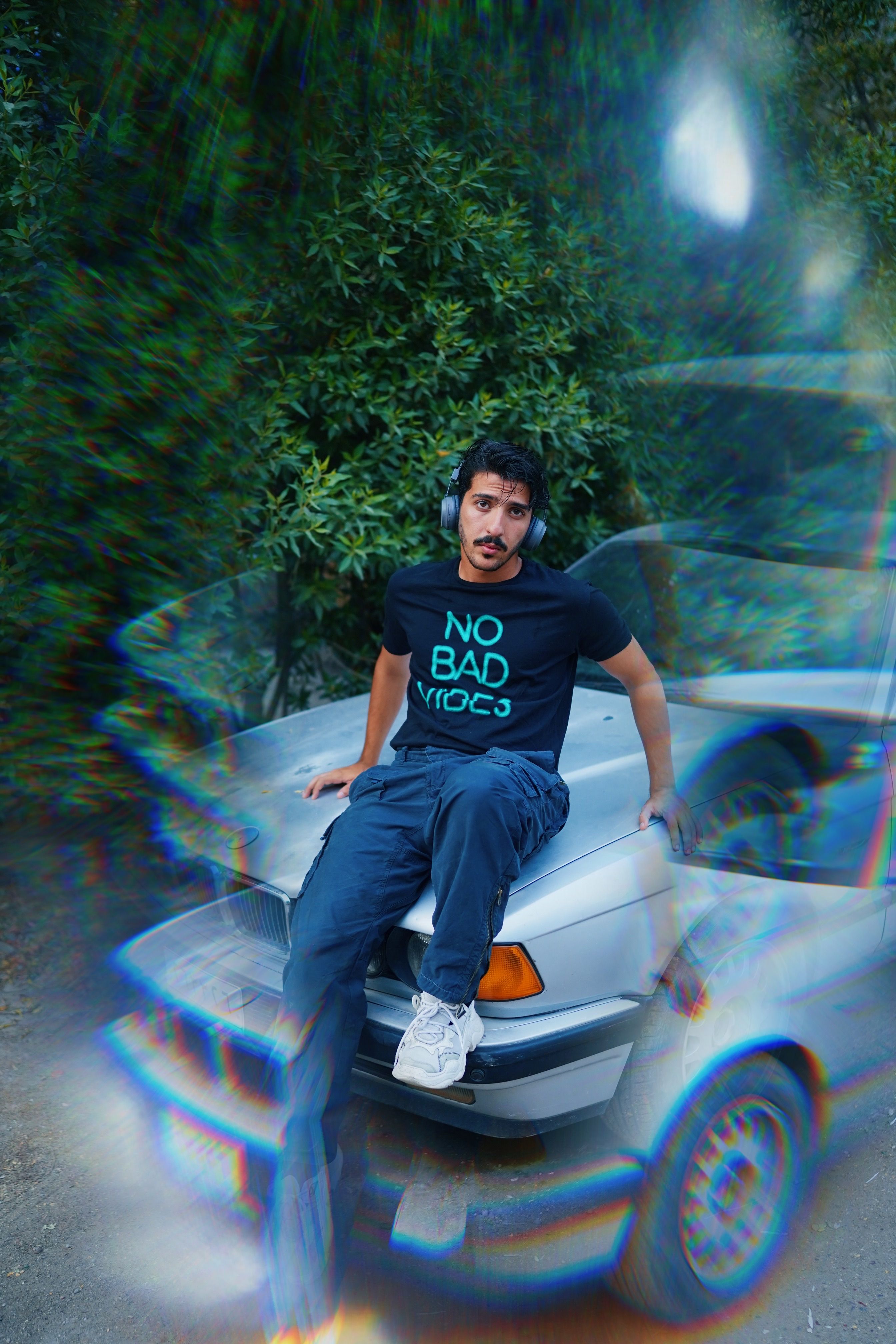 Young man sitting on car hood wearing headphones and casual attire