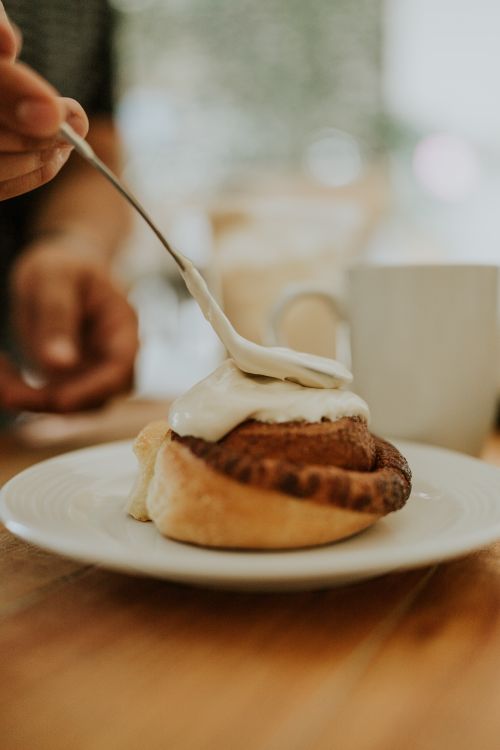 Free Close-up of cinnamon roll being topped with cream, perfect for food lovers. Stock Photo