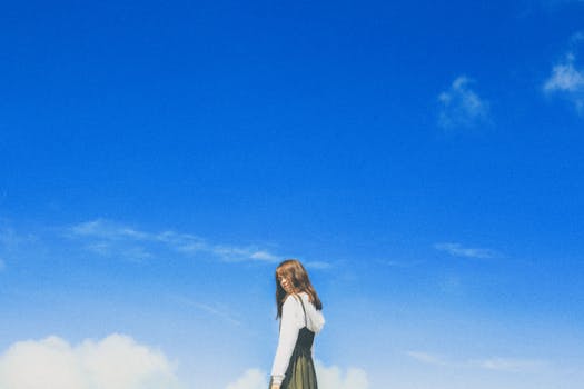 A young woman poses stylishly under a vibrant blue sky, embodying youthful fashion and freedom.