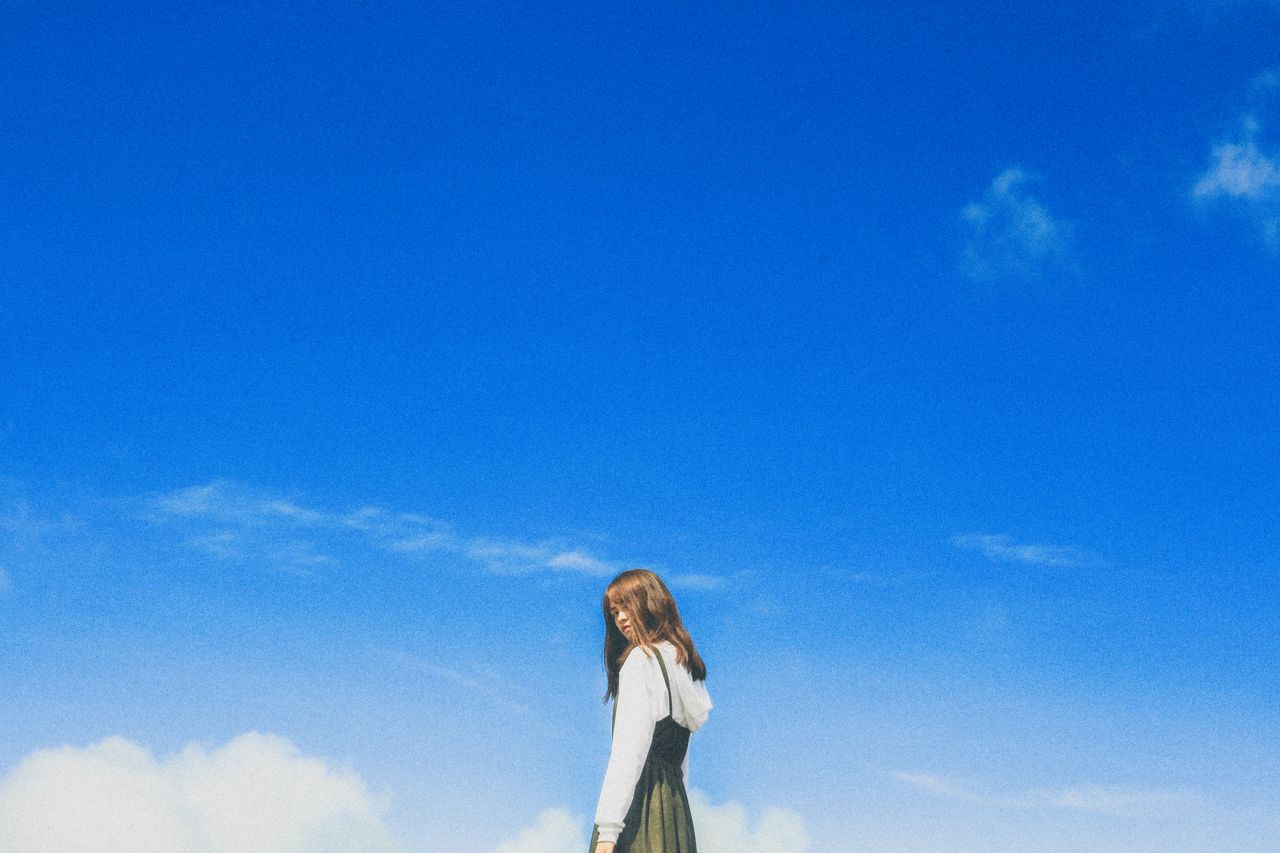a young woman poses stylishly under a vibrant blue sky embodying youth