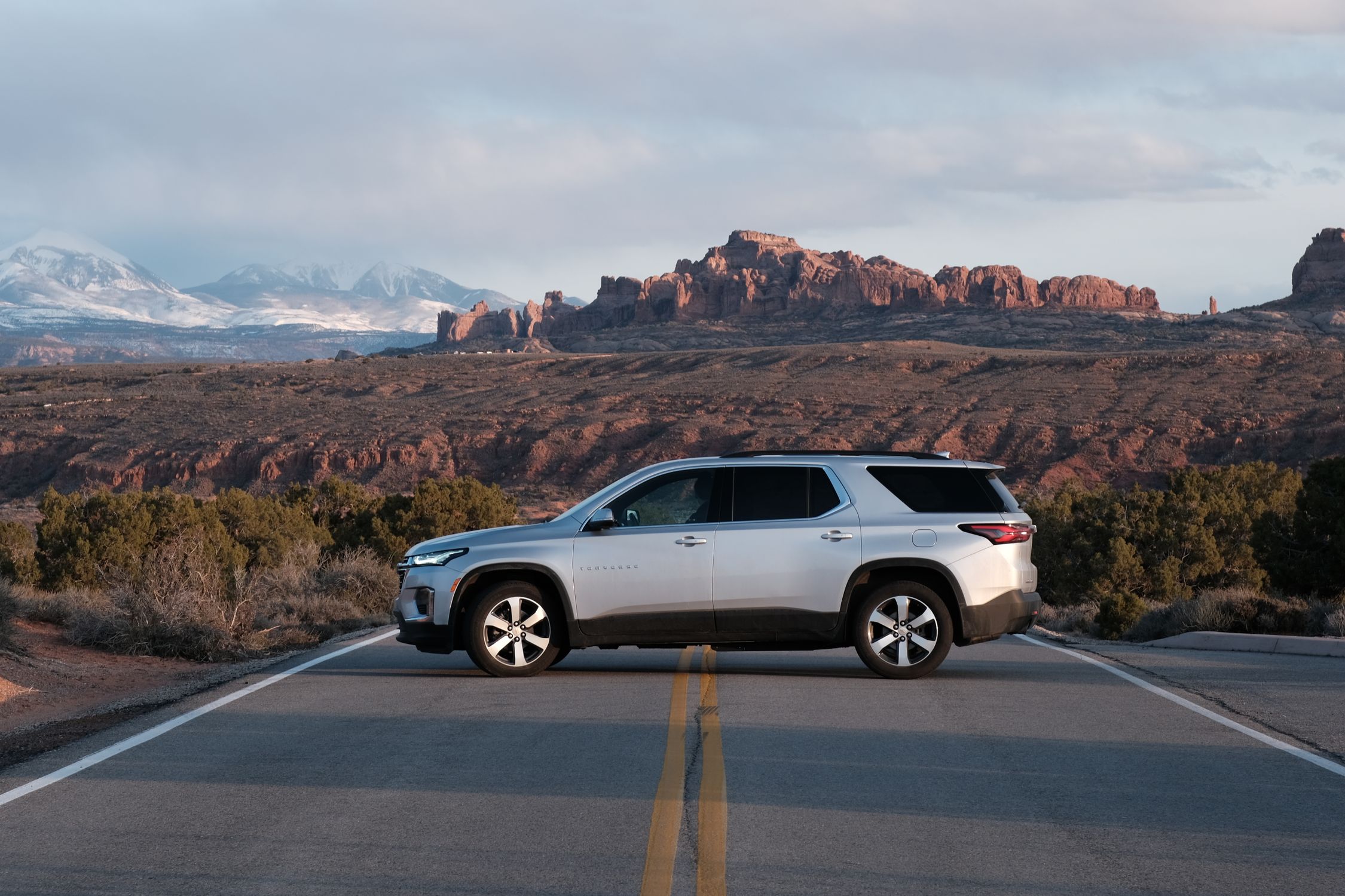 Silver SUV on a road against the rugged landscape of Moab, Utah, with red rock formations in the background.