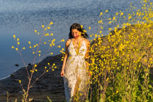 Brunette Woman in White Dress among Flowers on Lakeshore