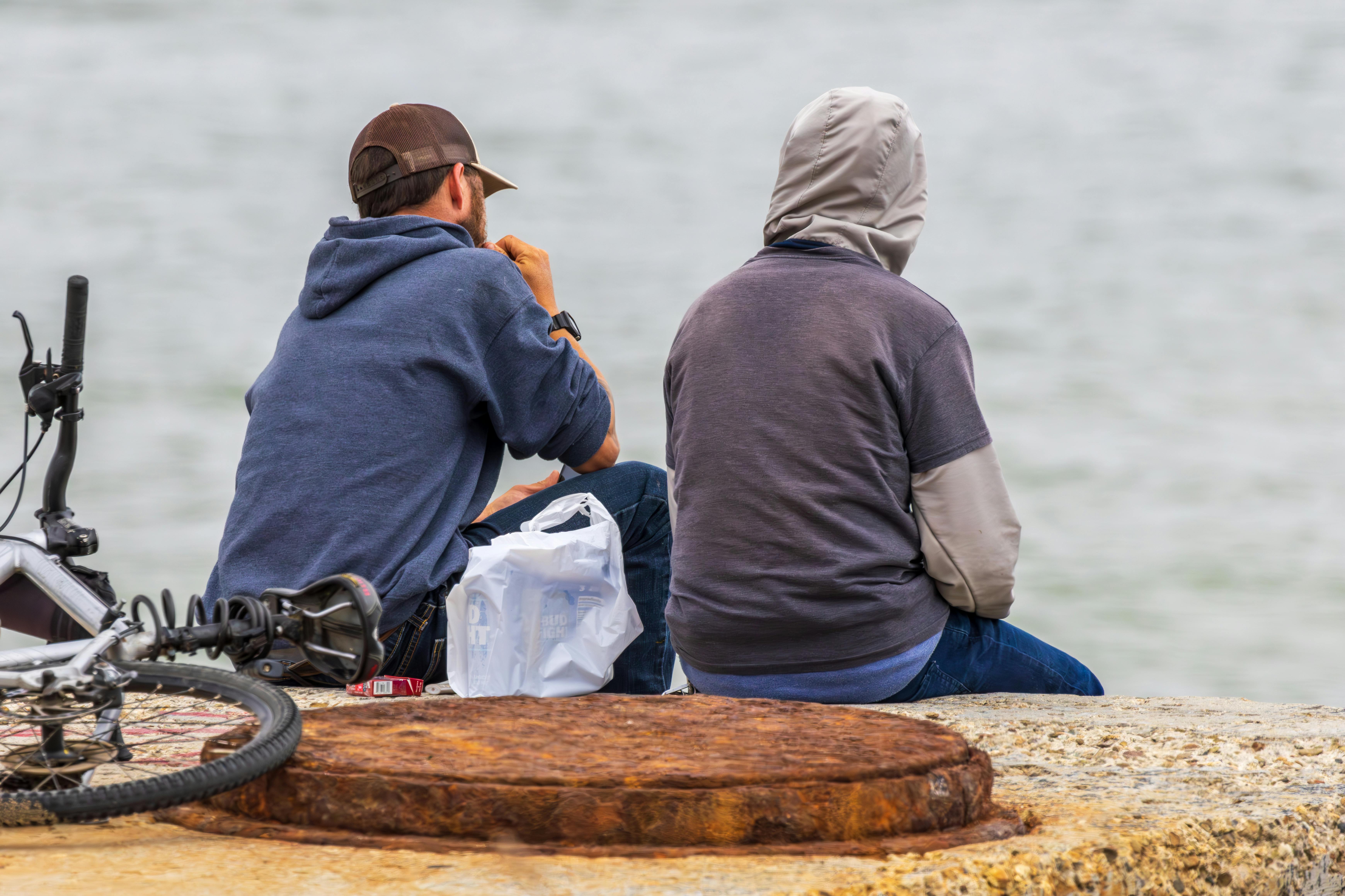 Two men sit together by the sea with a bicycle, enjoying the peaceful atmosphere.
