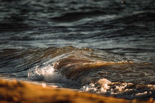 Free Close-up view of an ocean wave capturing the warm, golden hues of a sunset, highlighting natural beauty. Stock Photo