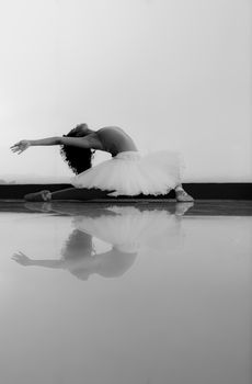 Graceful ballerina stretching in monochrome reflection shot, showcasing elegance and poise.