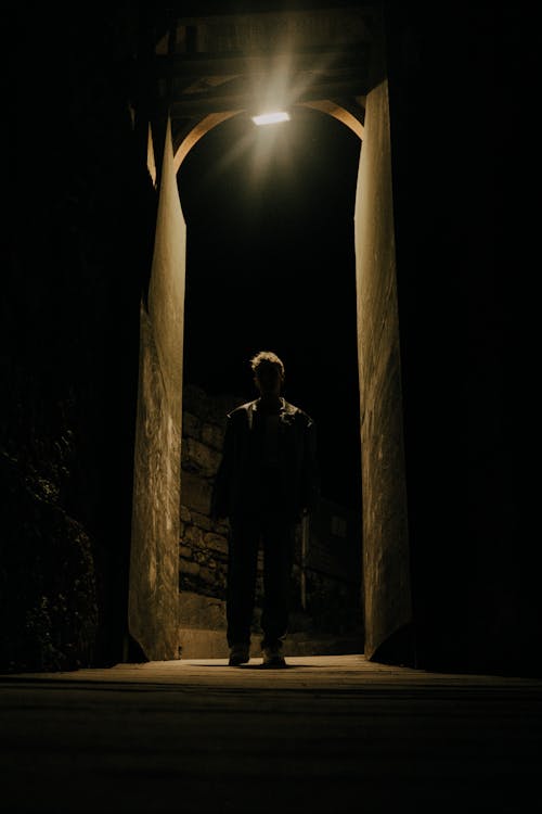 Light over Man Standing in Dark Alley at Night