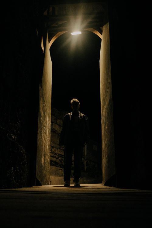 Free Silhouetted figure in a narrow, dimly lit urban alley at night, creating a mysterious ambiance. Stock Photo