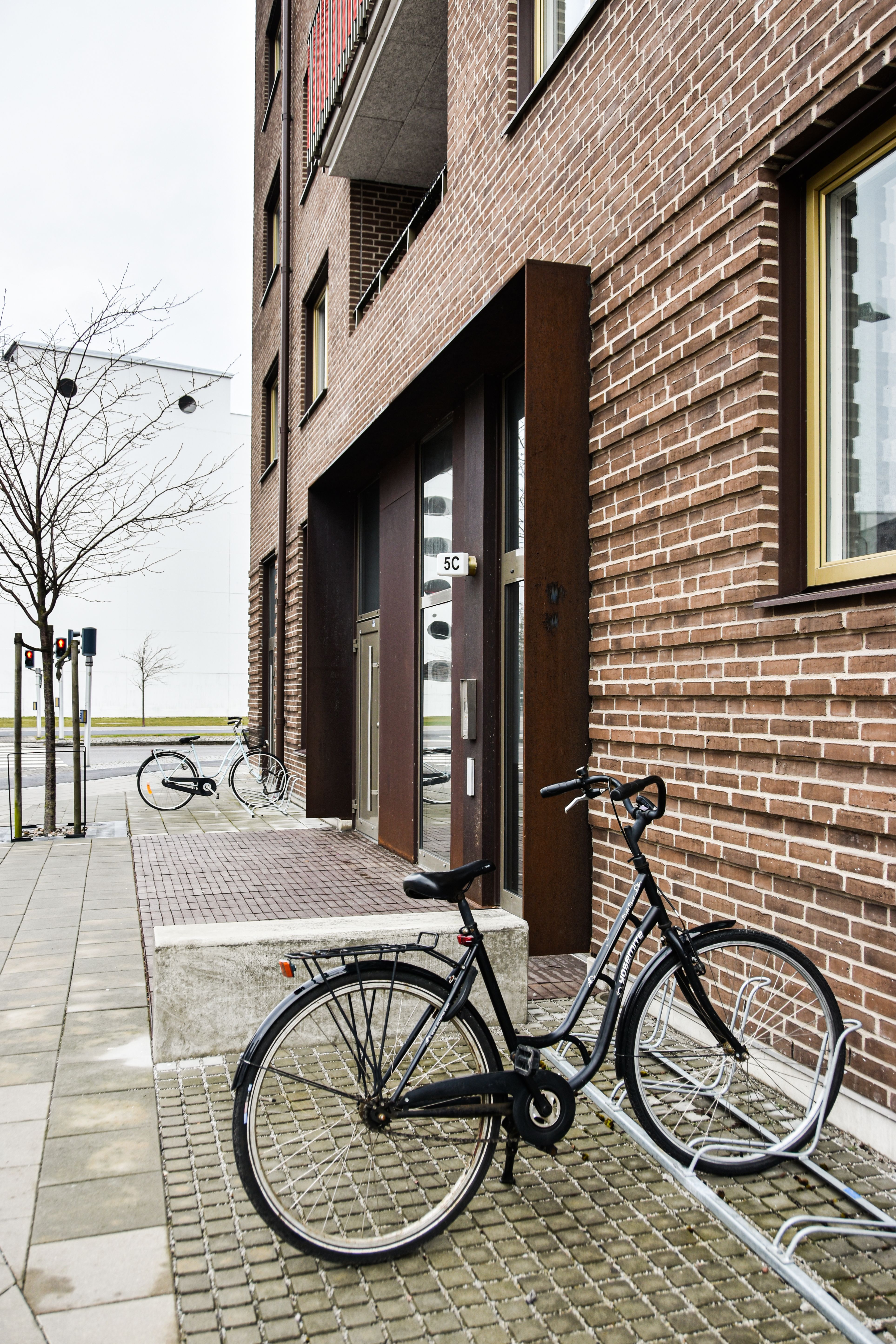 Sidewalk view of a brown brick building with bicycles. Modern urban environment.