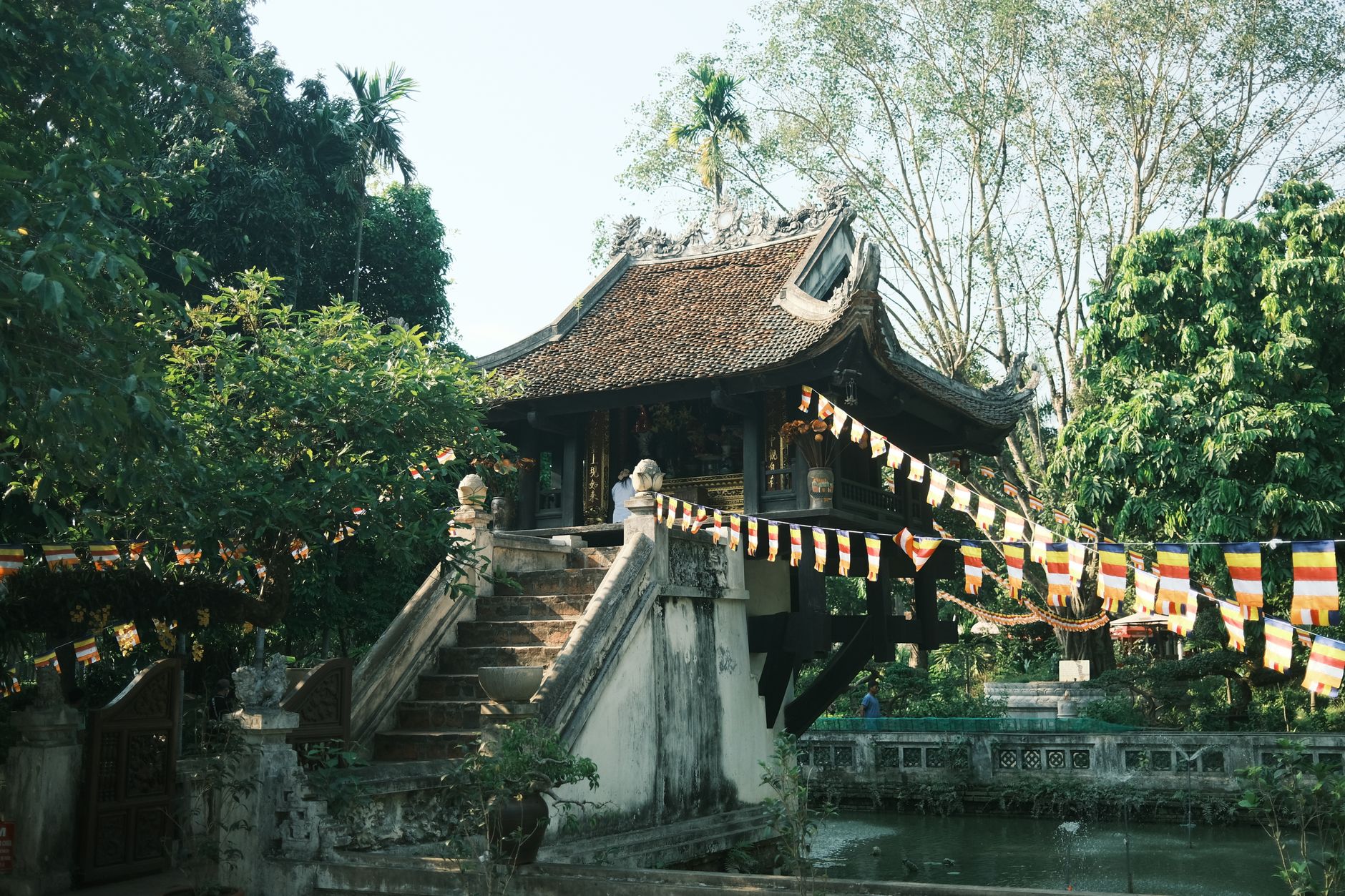 The historic One Pillar Pagoda in Hanoi surrounded by lush greenery and flags in summer.