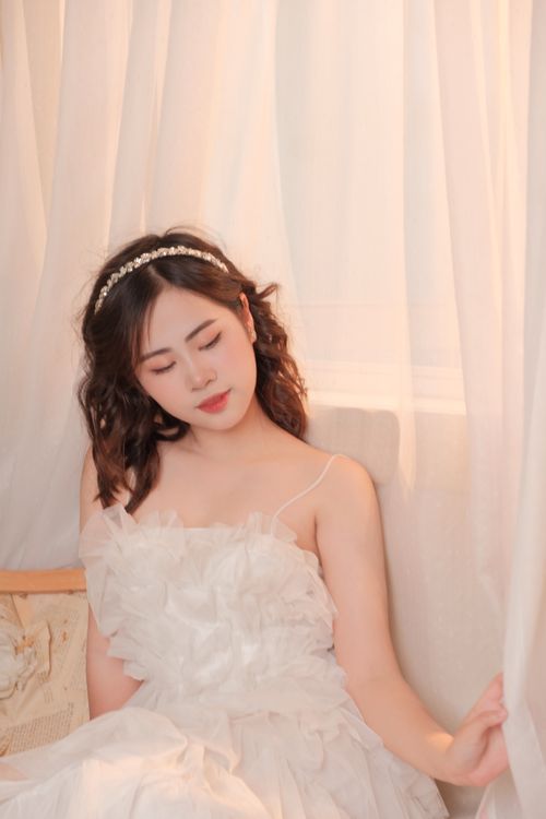 Free A young woman posing elegantly in a white tulle dress in a softly lit studio setting. Stock Photo