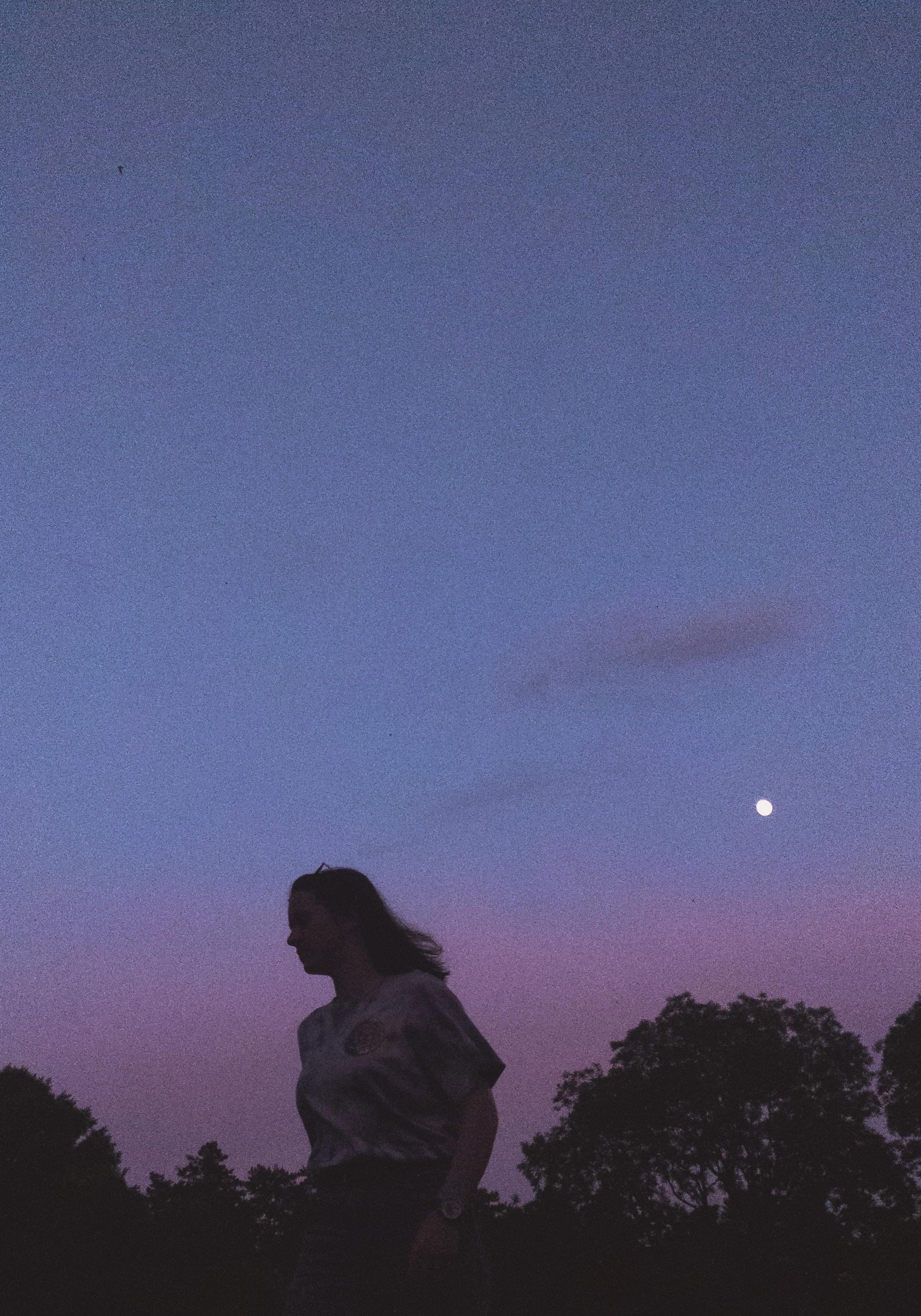 A serene image showcasing a woman's silhouette against a twilight sky marked by pink and blue hues, with the moon visible.