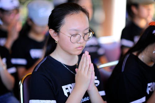 Woman in Eyeglasses with Eyes Closed and Hands Clasped