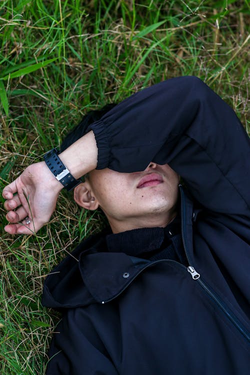 Free Young Man Lying on the Grass Field and Holding His Arm over His Eyes  Stock Photo