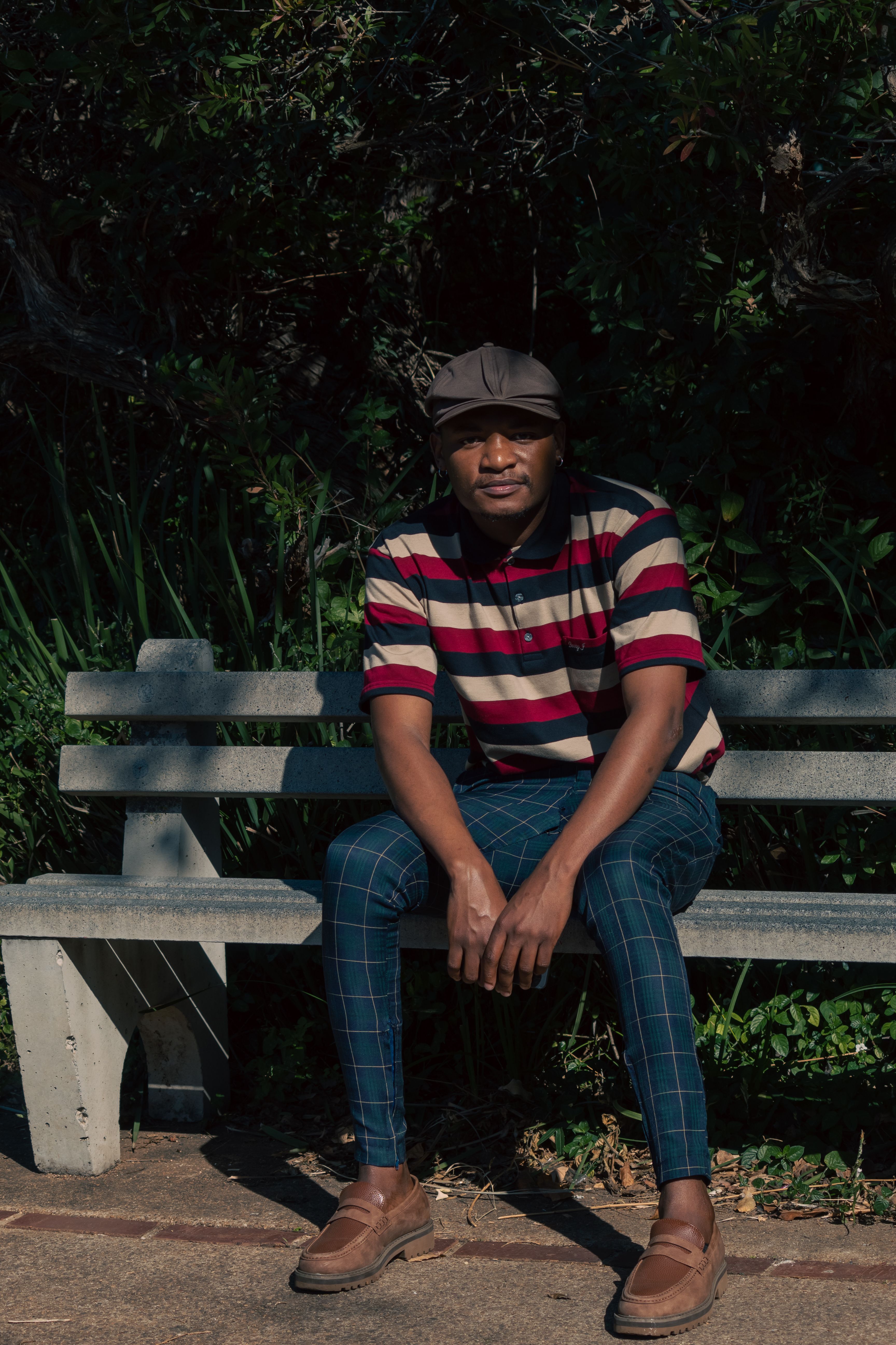 Casually dressed man sitting on a sunlit park bench enjoying the outdoors.