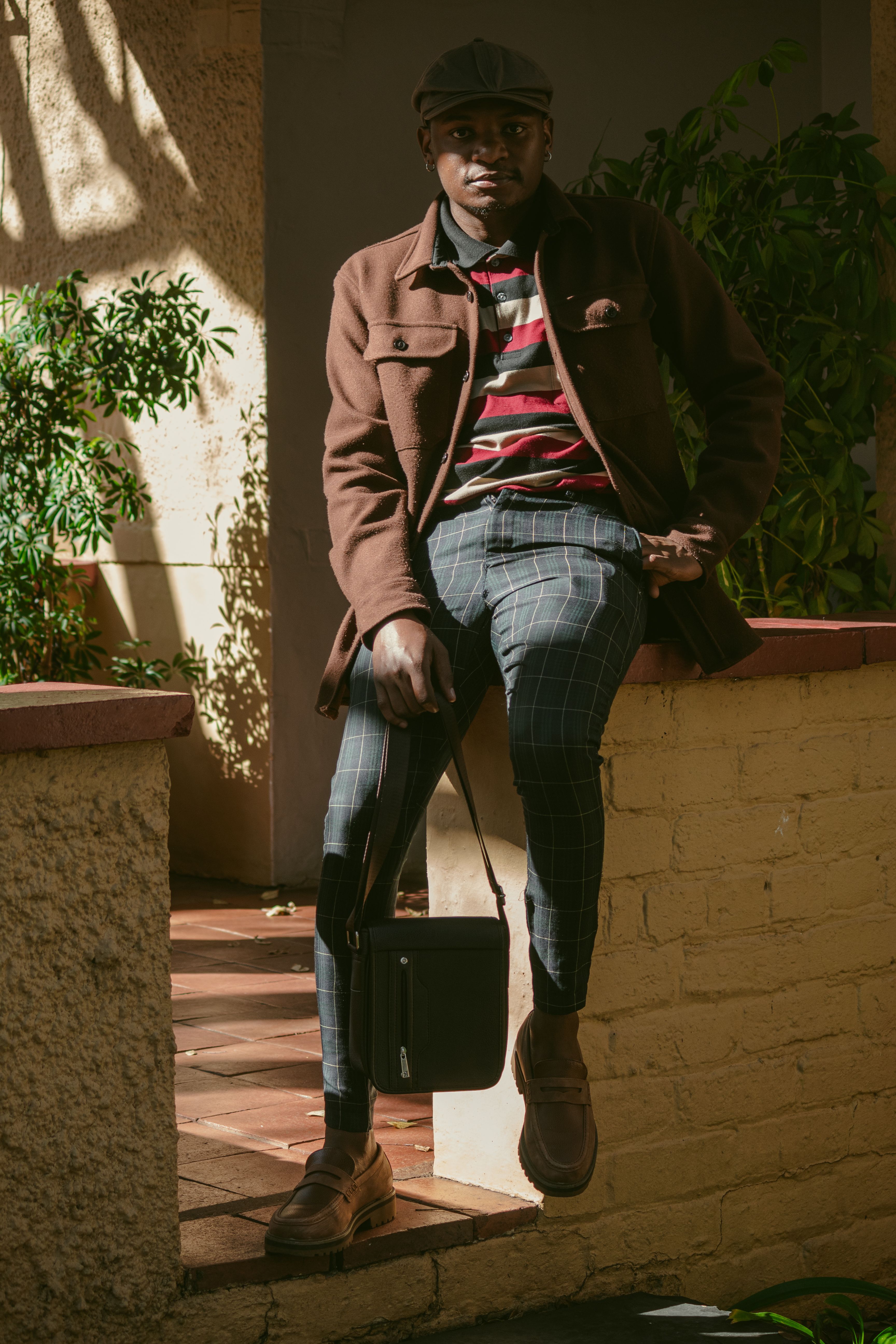 Young man with cap and plaid pants stylishly posing outdoors, displaying fashion trends.