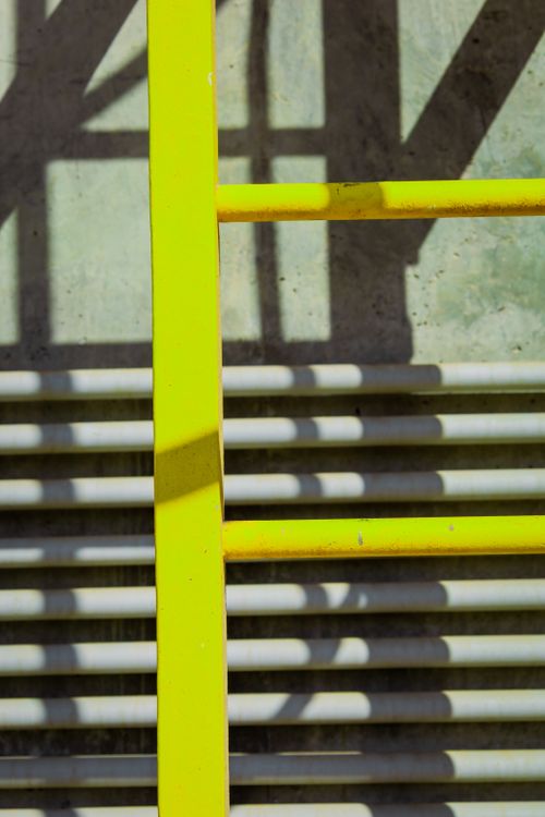 Free Close-up of a yellow ladder casting shadows on a textured industrial surface, conveying safety and industrial themes. Stock Photo