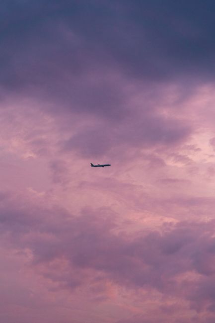 Silhouetted airplane flying against a vibrant pink and purple cloudy sky during sunset.