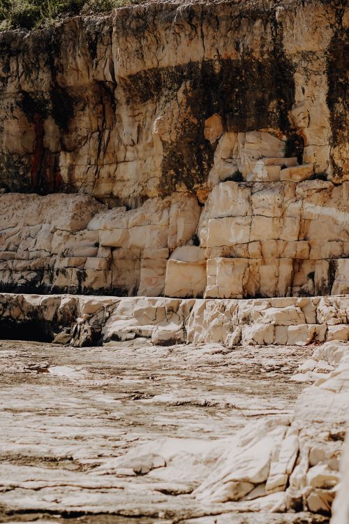 Free Stunning vertical view of a rugged cliff with weathered rock formations by the sea, capturing natural beauty and texture. Stock Photo