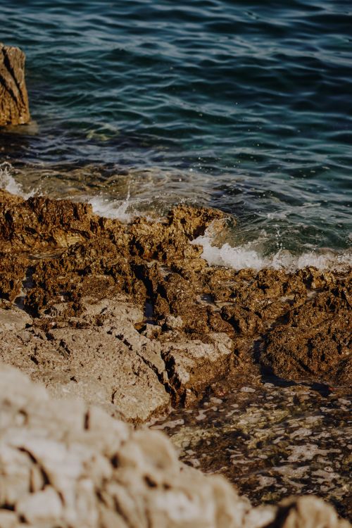 Free Vibrant coastal scene featuring rugged rocks, clear waves, and deep blue sea. Stock Photo
