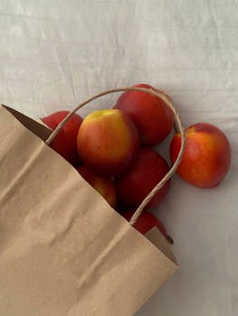 Top view of fresh red apples spilling out of a craft paper bag on a white background.