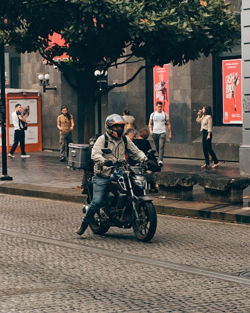 Man Riding a Motorcycle with a Trunk on a Cobblestone Street