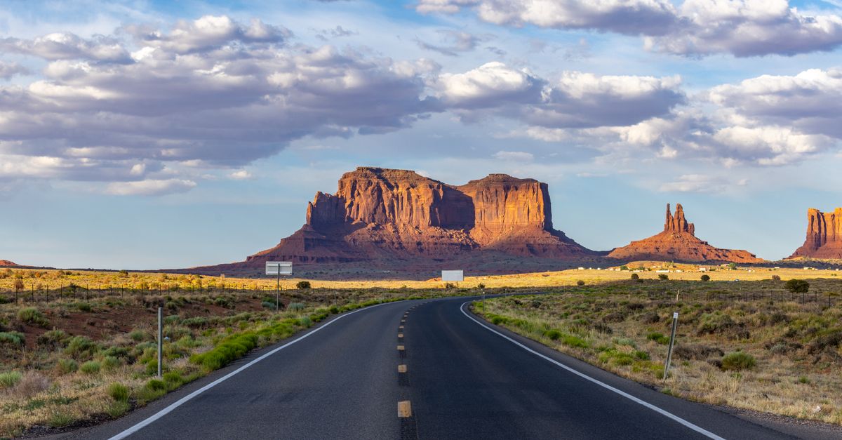 A picturesque road leading to Monument Valley with stunning sandstone formations under a vibrant sky.
