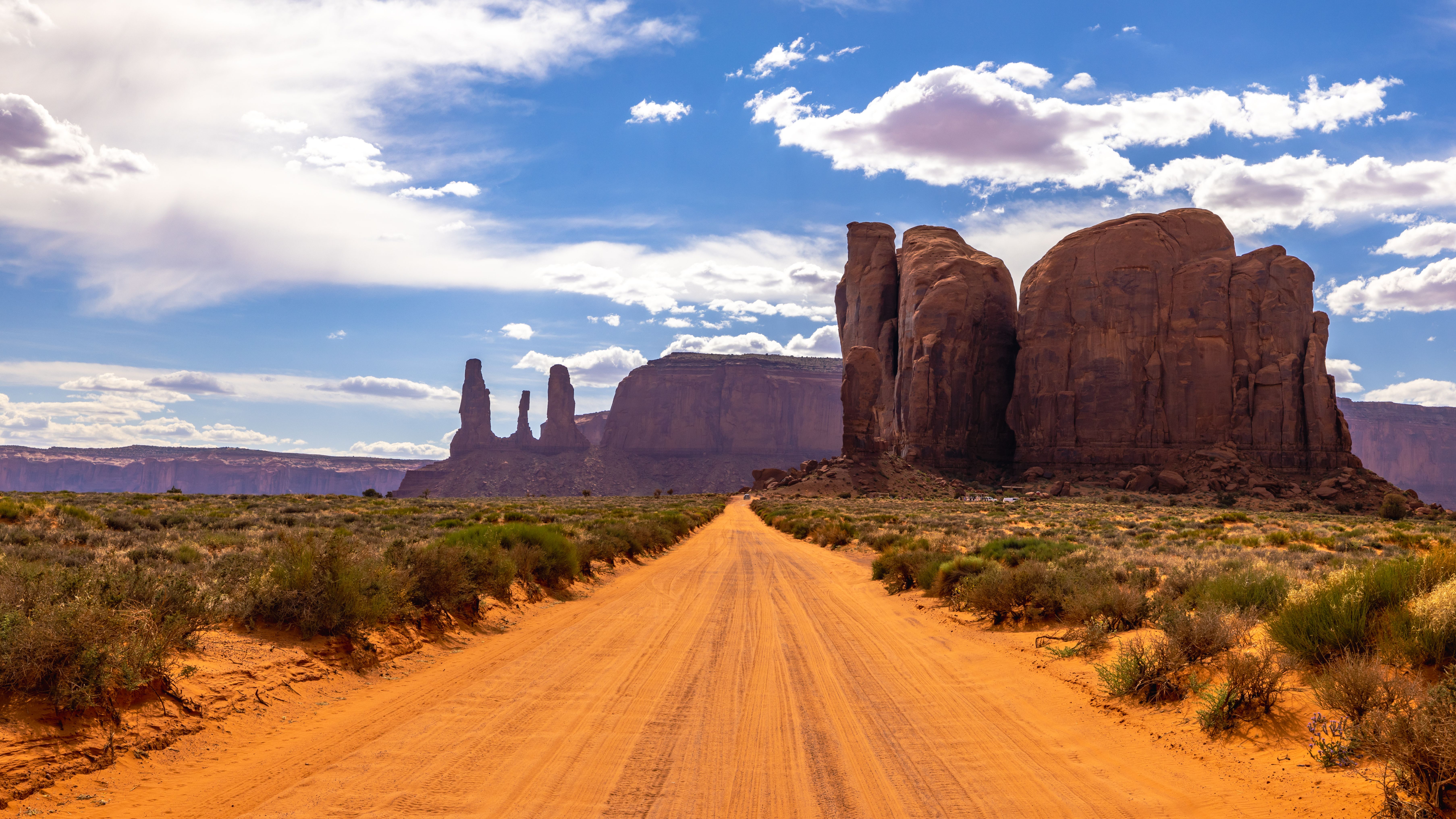 Breathtaking view of Monument Valley with towering rock formations under a bright, partly cloudy sky.