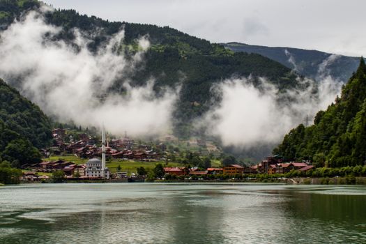 Scenic view of Uzungöl lake with mosque, nestled in misty mountains. Captivating natural landscape.