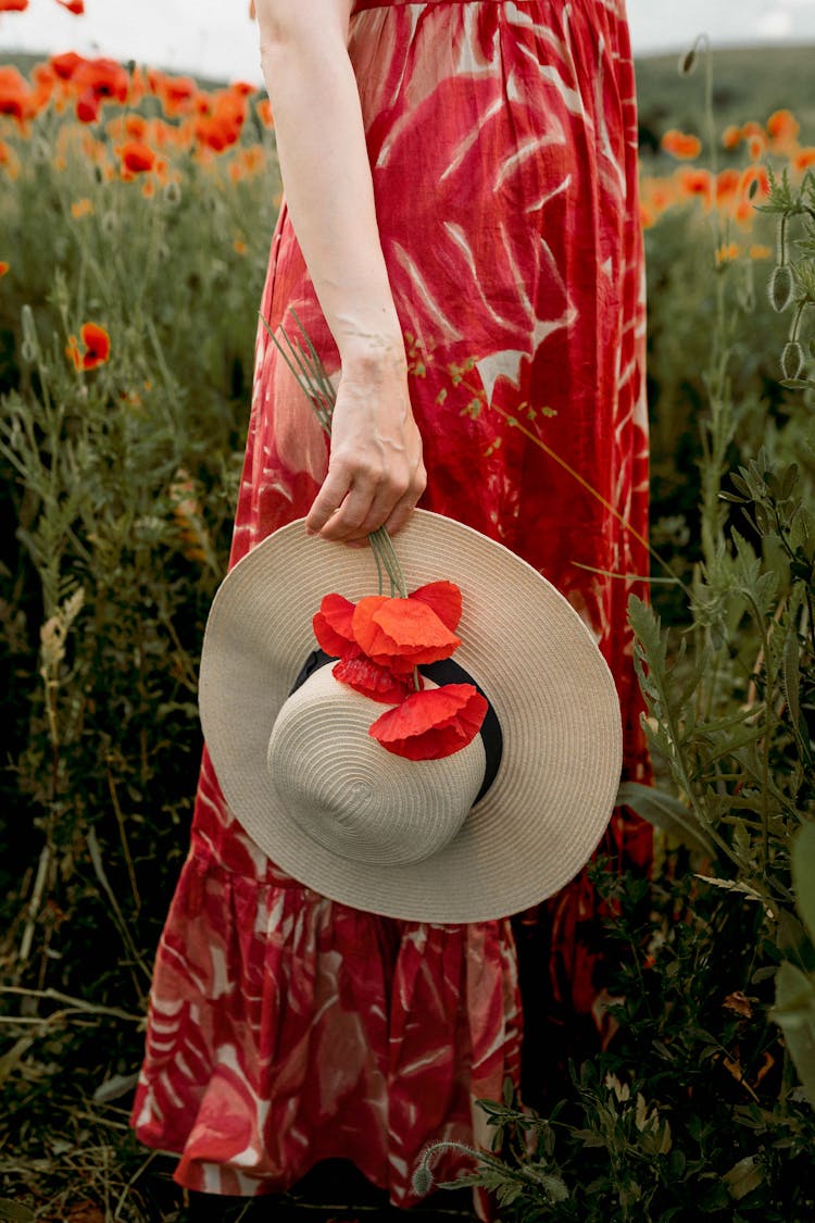 Closeup Of A Woman Wearing Red Floral Dress Holding A Summer Hat In A Poppy Field