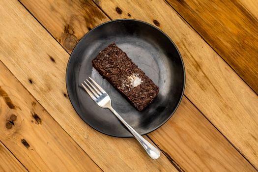 Delicious chocolate brownie served on a black plate with a fork on a rustic wooden table.