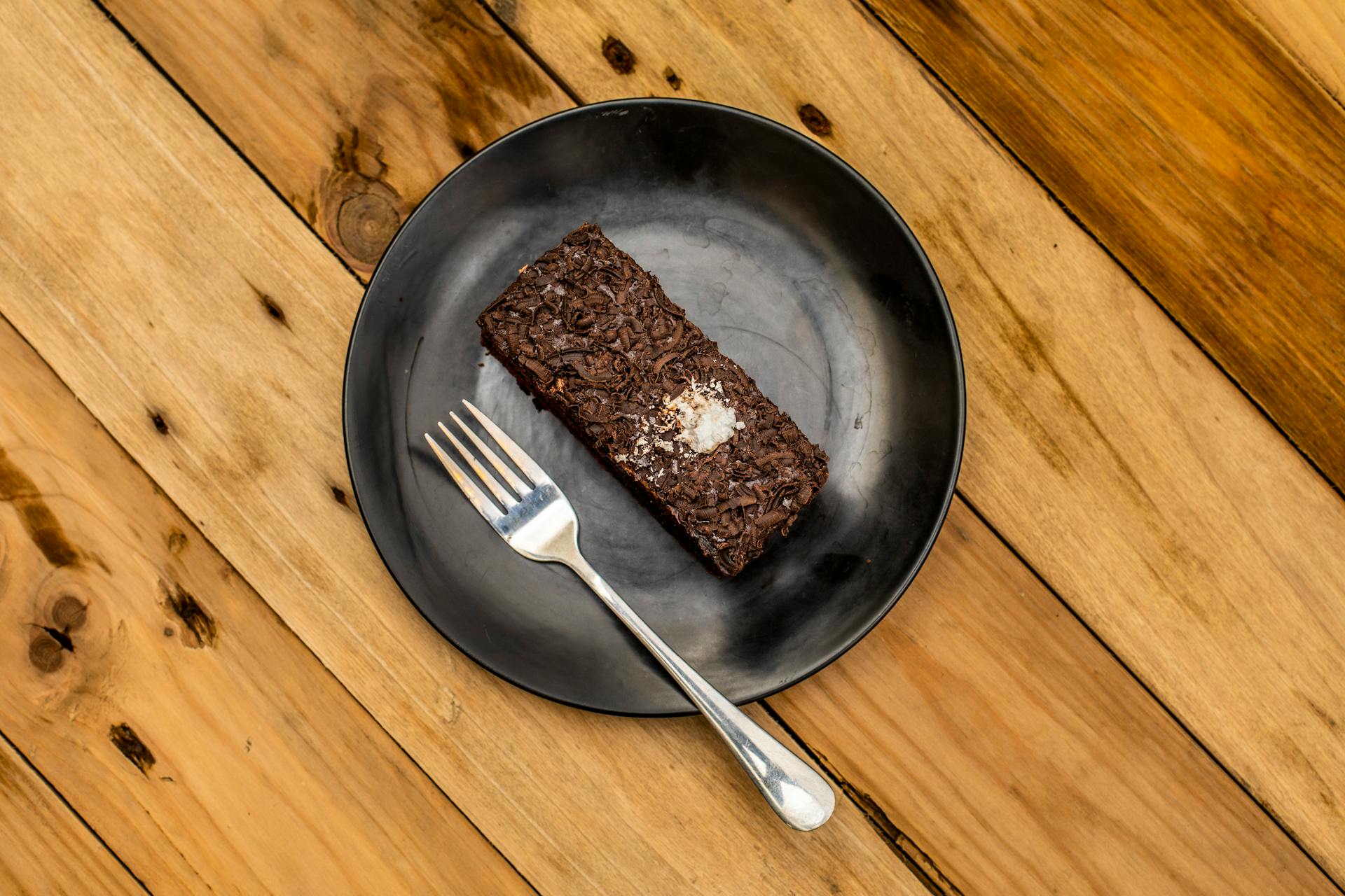 Delicious chocolate brownie served on a black plate with a fork on a rustic wooden table.