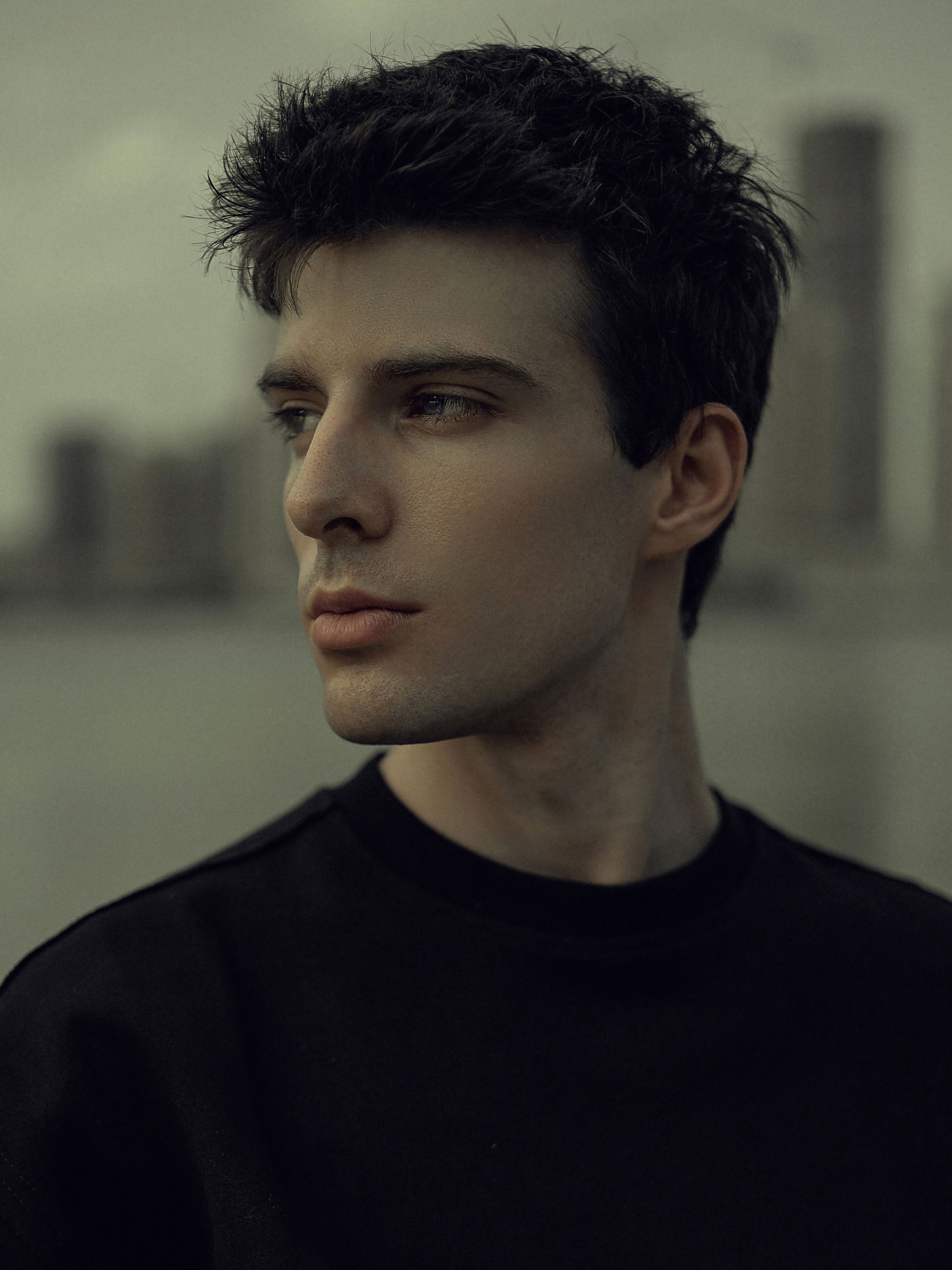 A dark and moody portrait of a young man in an urban setting, reflecting style and introspection.