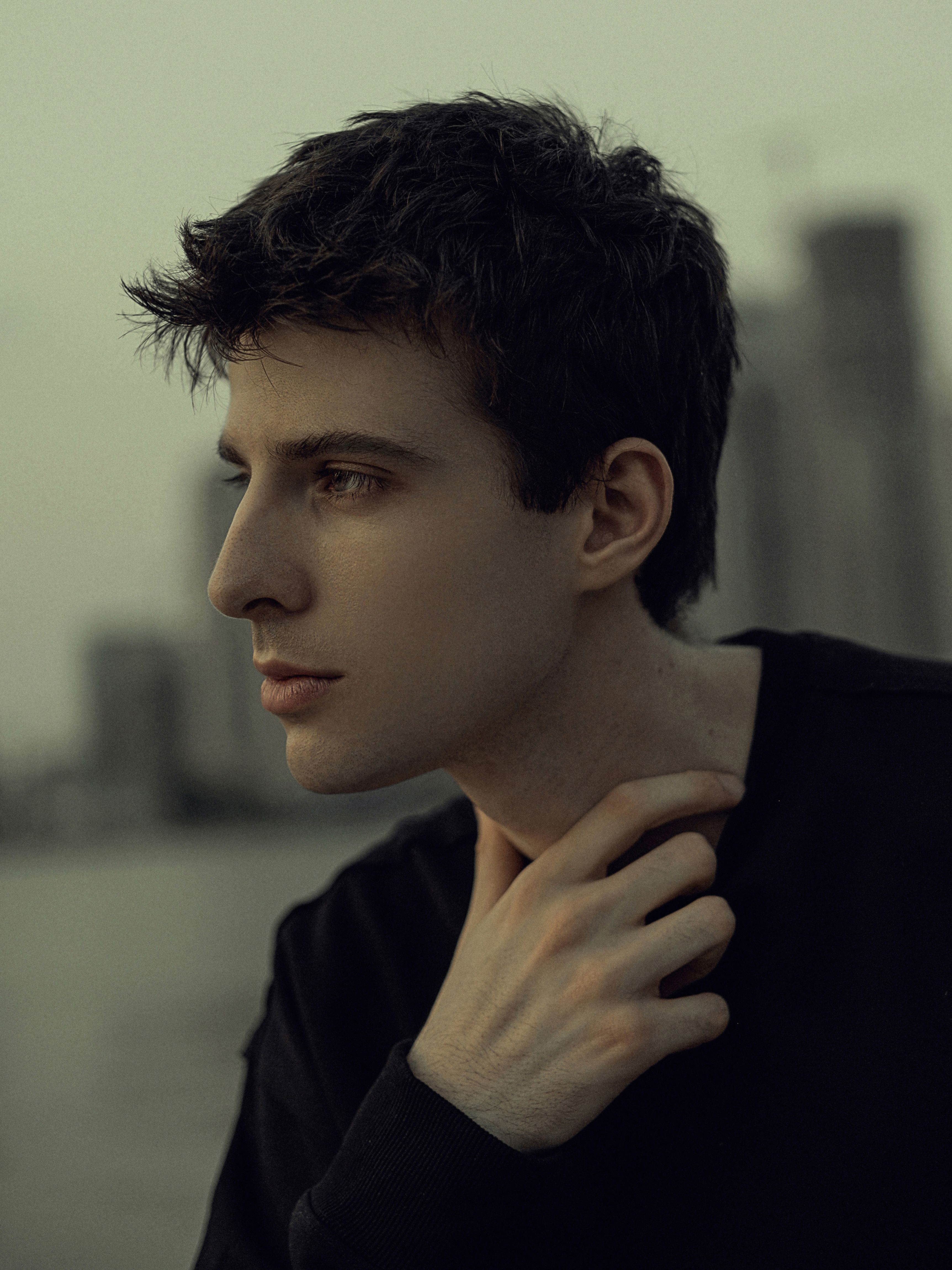 Profile portrait of a young man looking contemplative in an urban setting during the day.