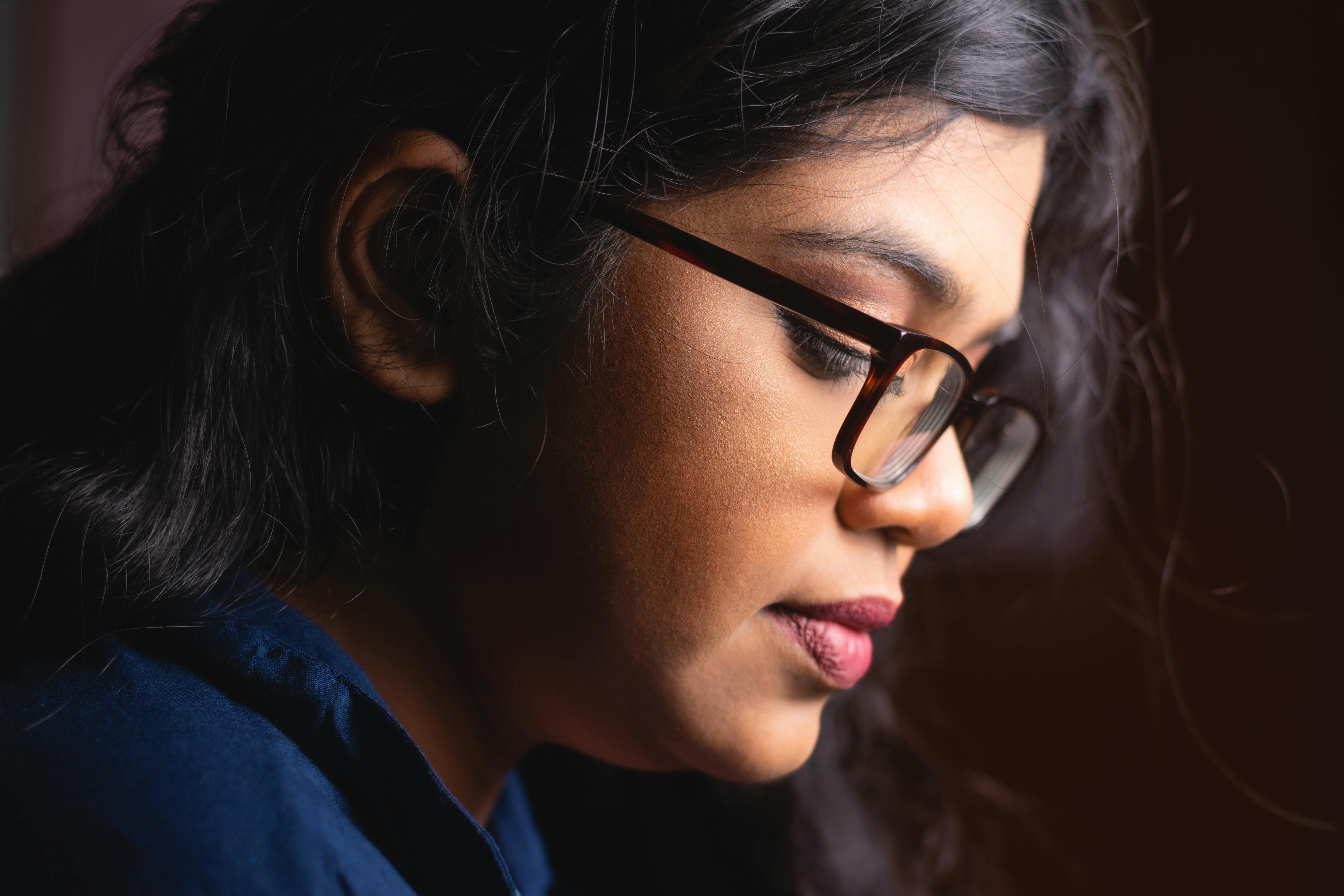 Close-up portrait of a thoughtful woman with eyeglasses, highlighting emotion.