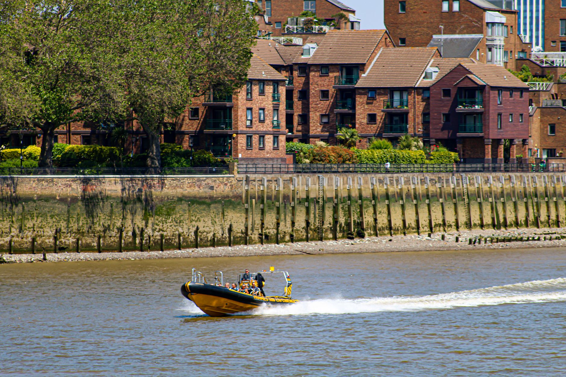 A speedboat cruises along the River Thames with urban buildings in London, England.
