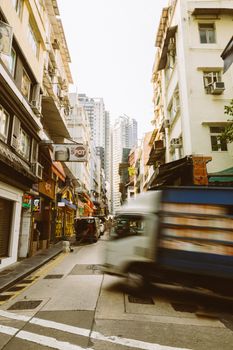 Dynamic view of a bustling urban street in Hong Kong with blurred motion of a moving truck.