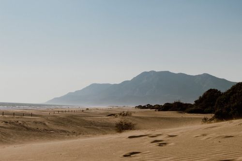 Free Peaceful sandy beach with mountain backdrop, ideal for tranquil nature scenes. Stock Photo