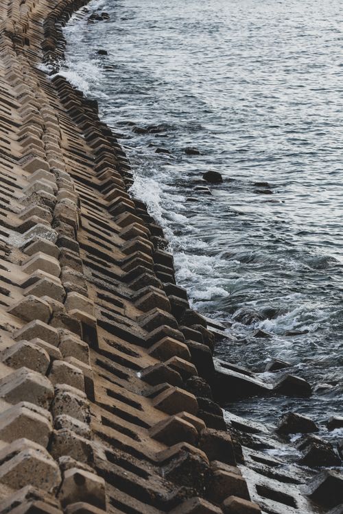 Free Aerial view of a textured concrete sea dike along a calm coastline, with gentle waves lapping against the shore. Stock Photo