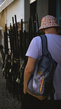 A stylish person in a bucket hat and backpack walking down city streets, showcasing urban fashion.