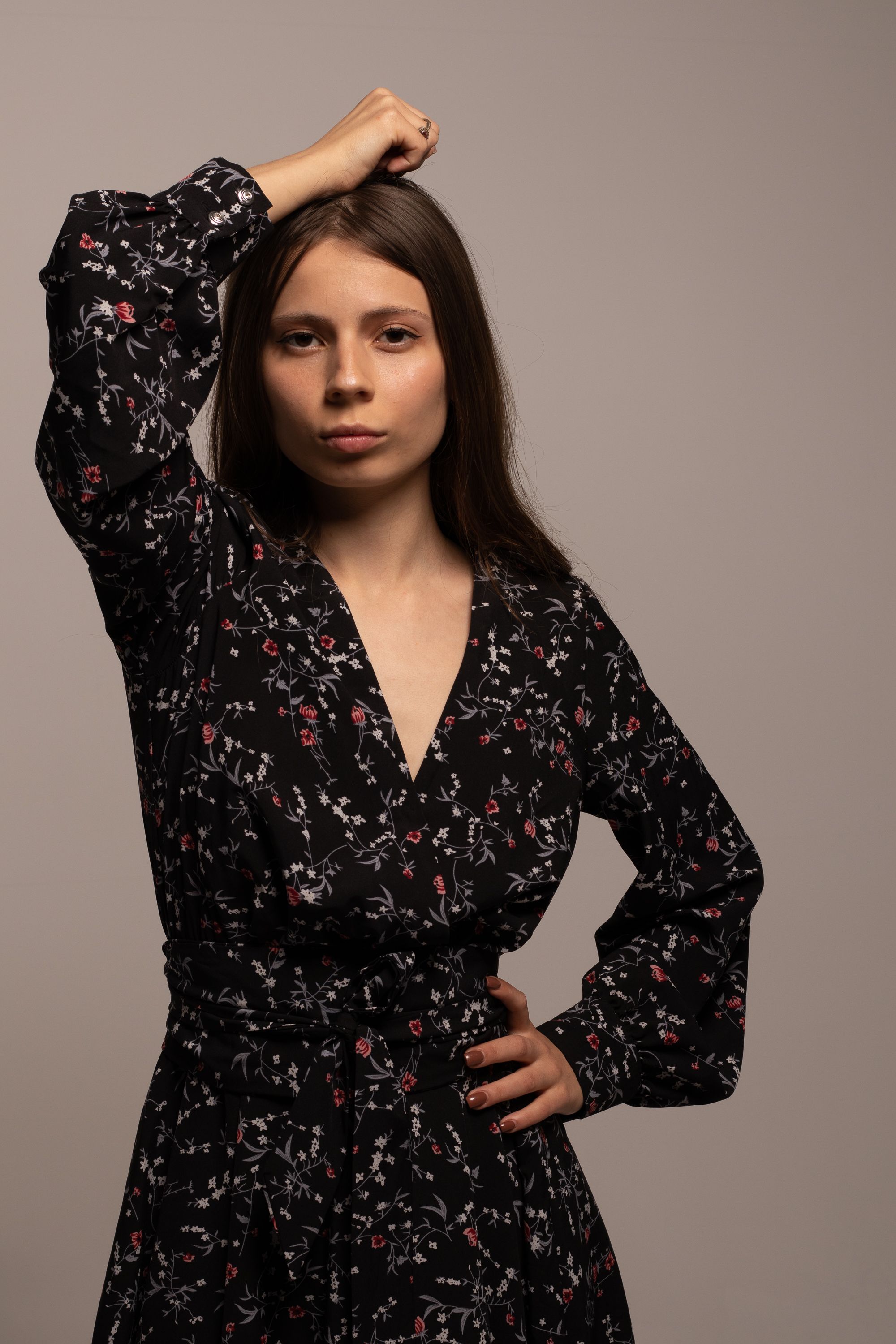 A stylish young woman poses confidently in a floral dress against a neutral background.