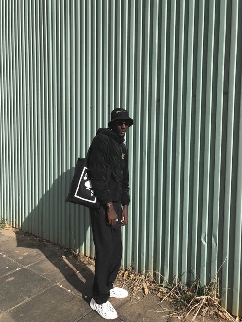 Stylish young man in black outfit and bucket hat outside.