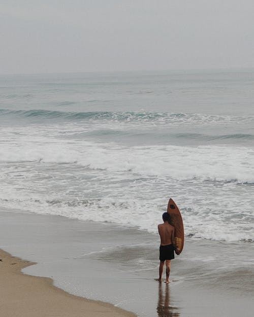 Back View of a Man with a Surfboard on the Beach 